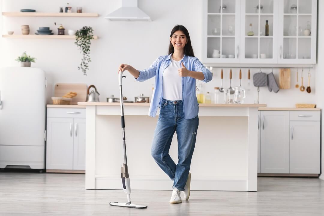 Happy woman in the kitchen holding a mop